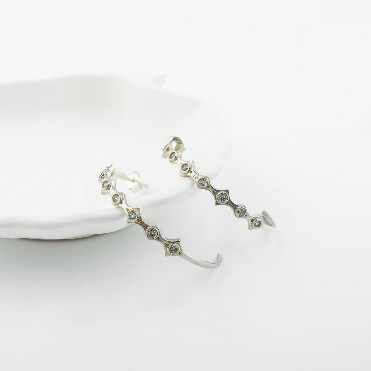 Silver diamond-shaped hoop earrings with CZ stones styled on model's ear