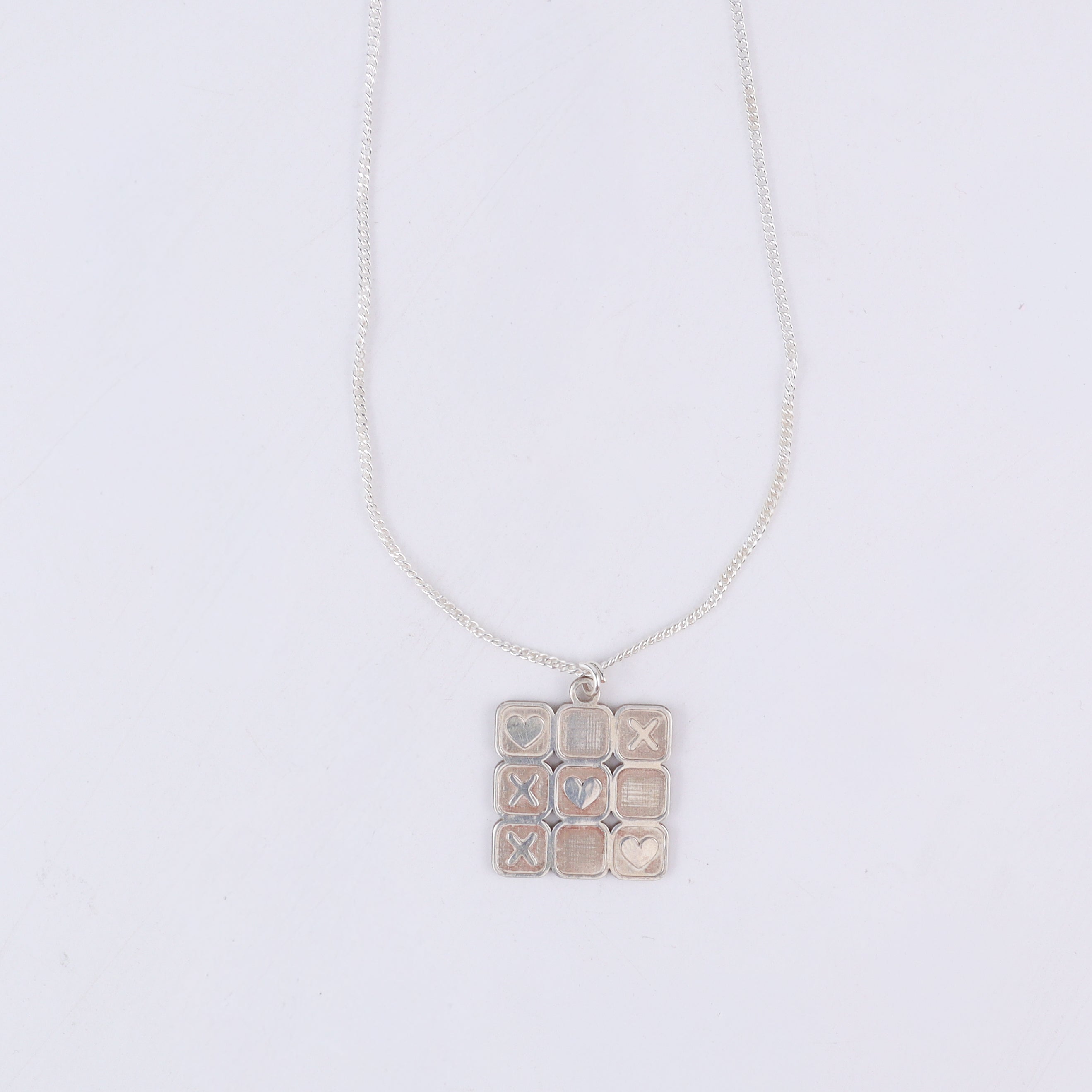 Close-up of tic tac toe grid detailing on silver pendant