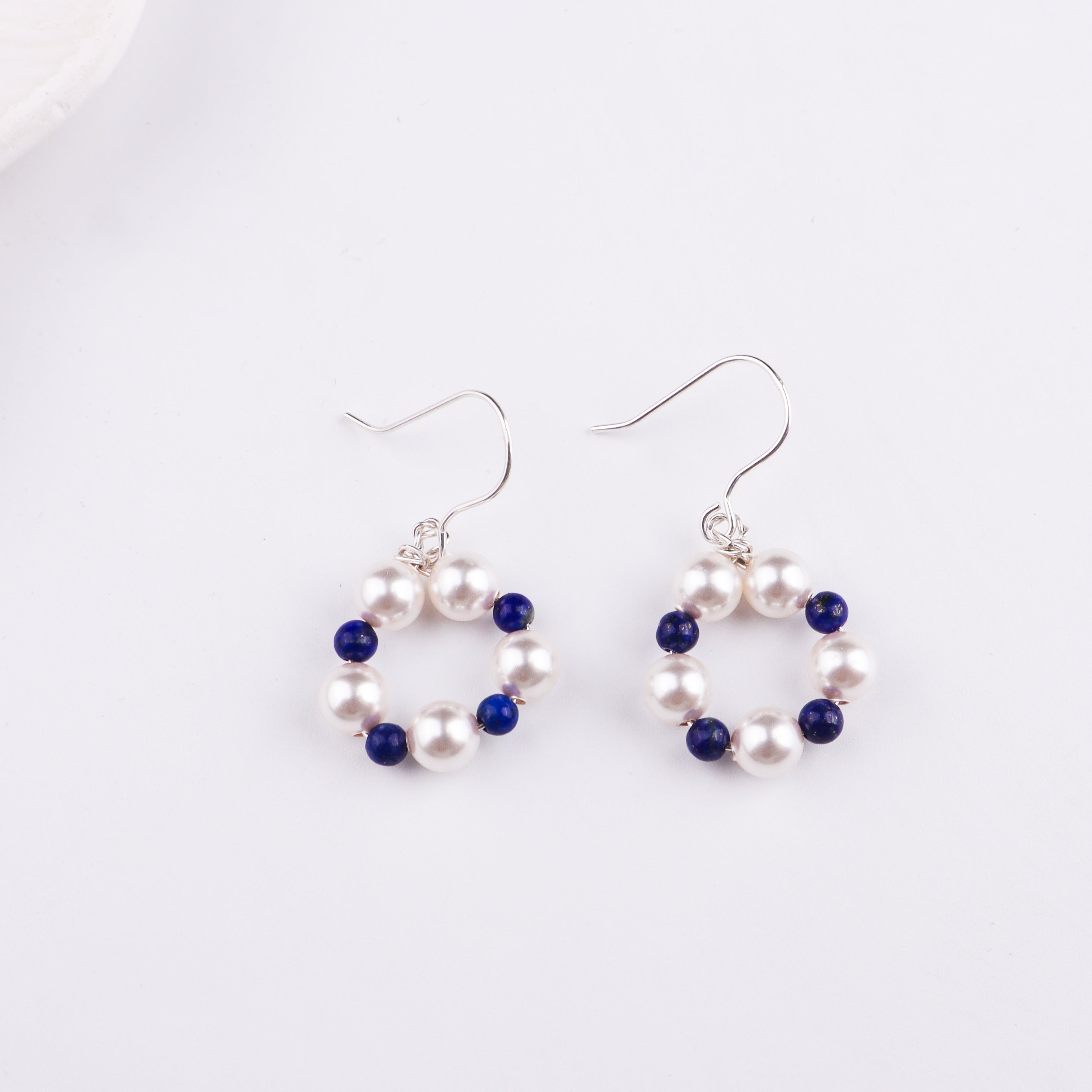 Pearl and lapis lazuli beaded earrings on white surface