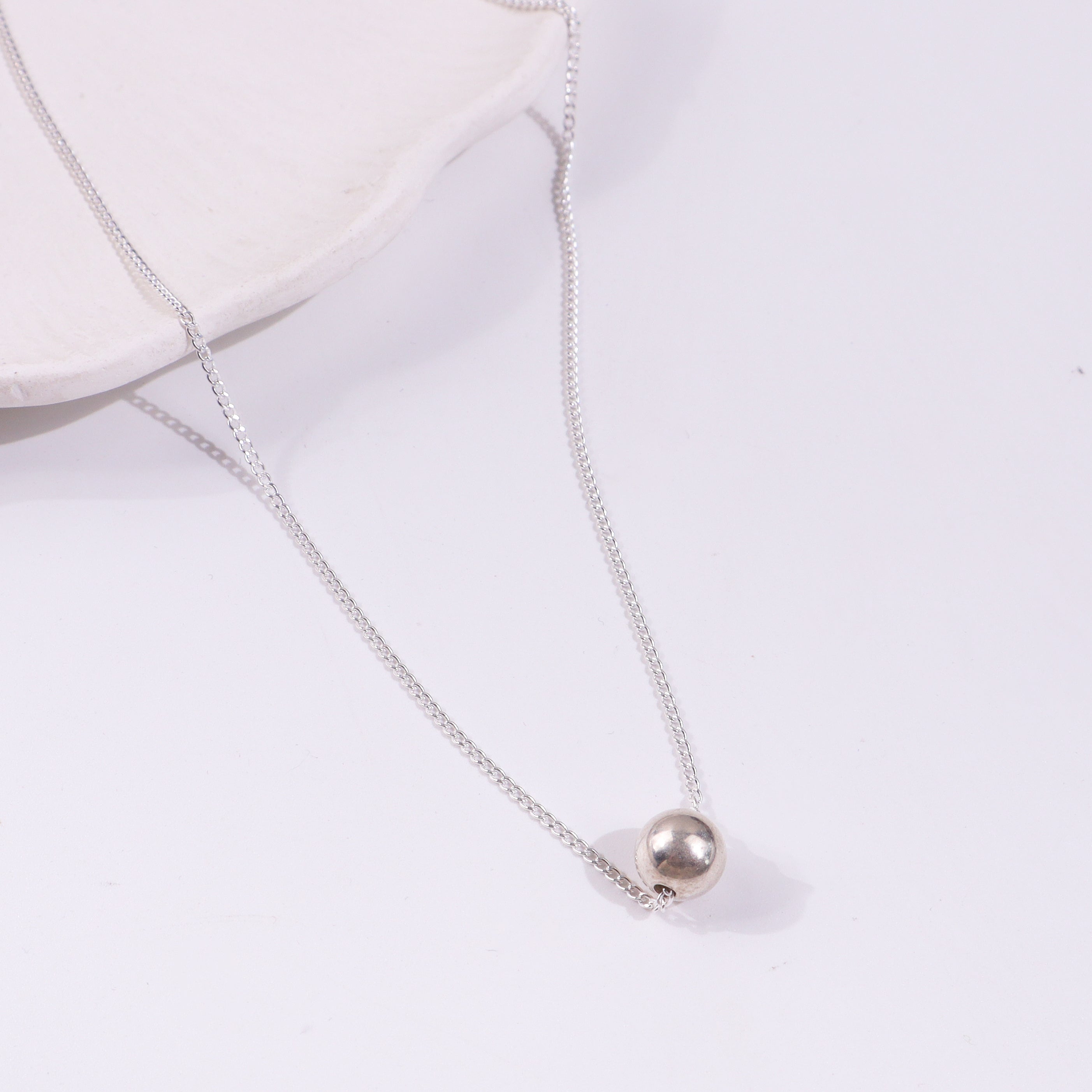 Silver chain necklace with bead pendant displayed on a white background