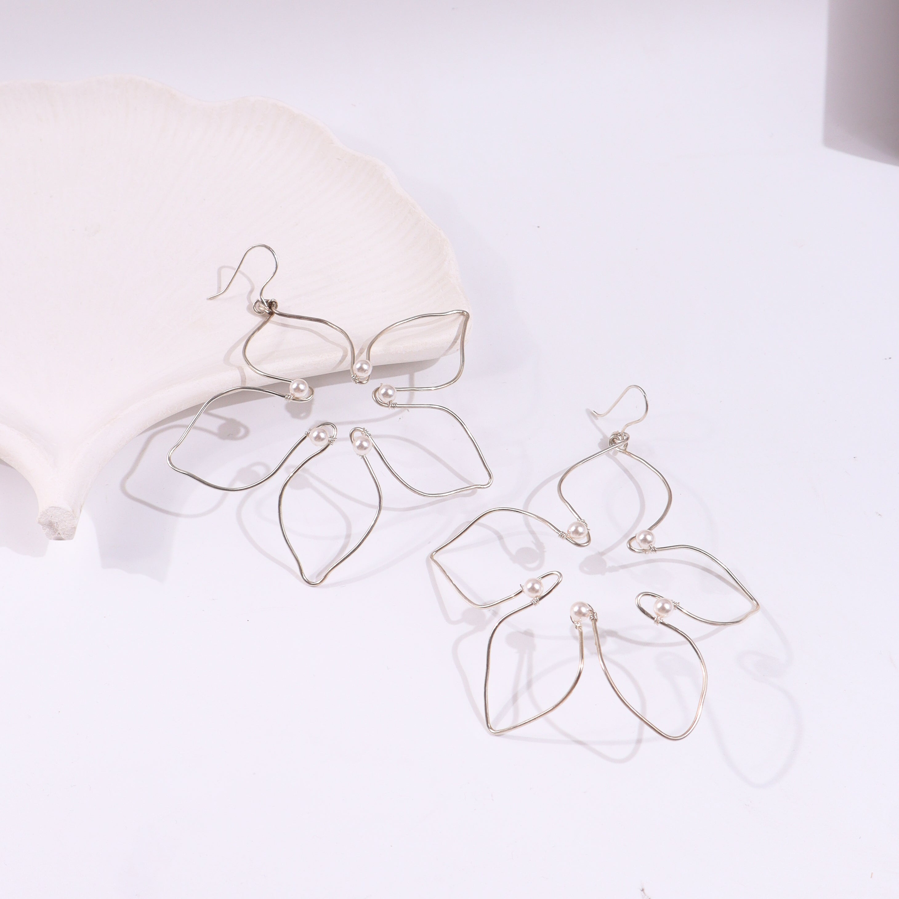 Silver pearl flower earrings on white shell