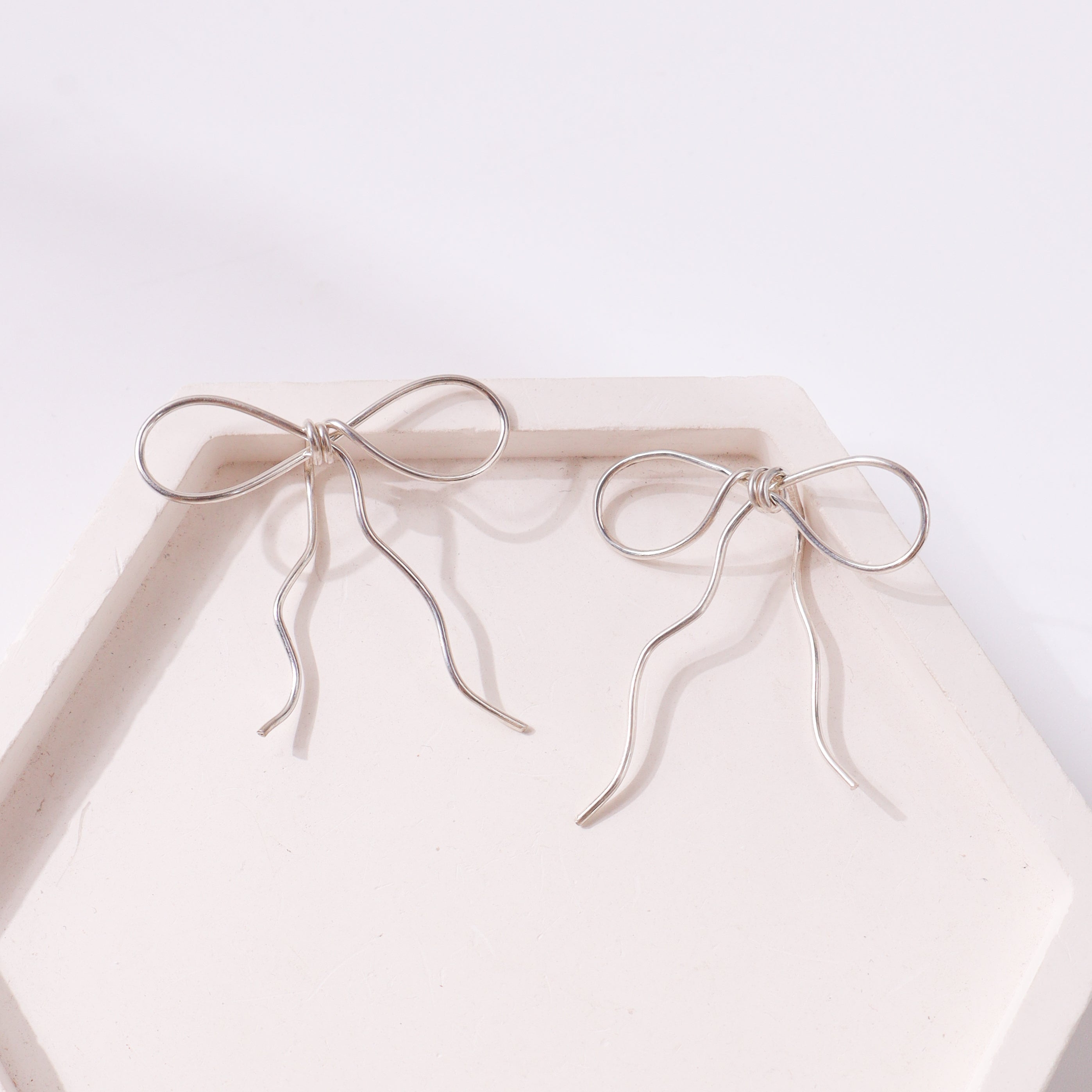 Silver bow earrings on white display
