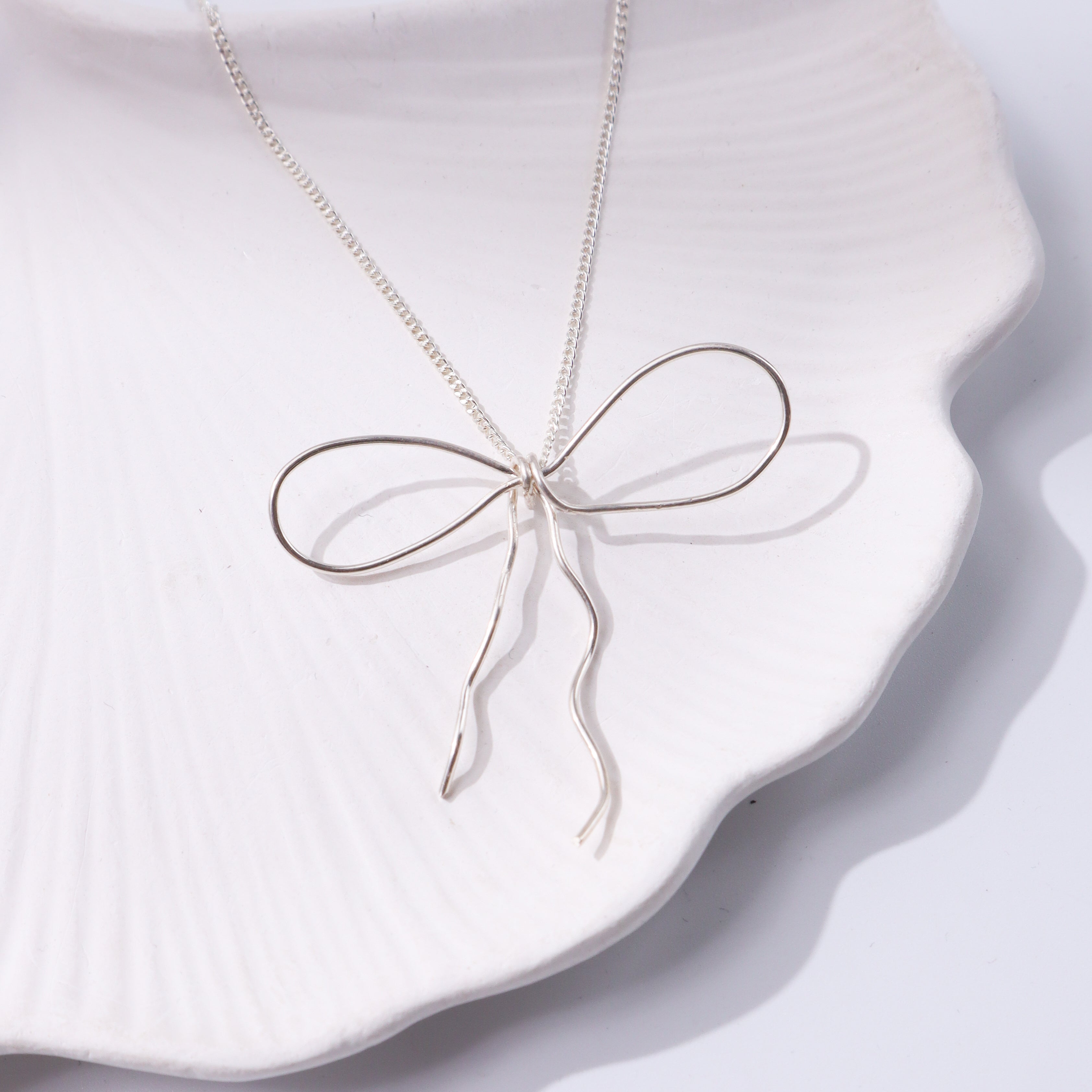 Silver bow necklace on white display