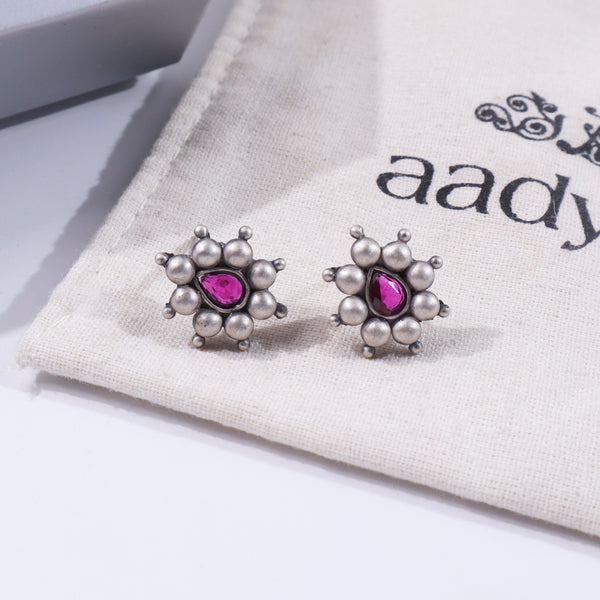 Silver drop-shaped earrings with pink gemstones on fabric background