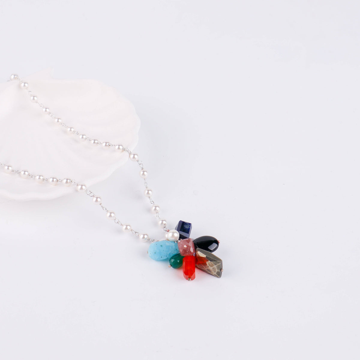 Flat-lay of multicolour stone bunch necklace with pearl Gantan on silk fabric and soft lighting
