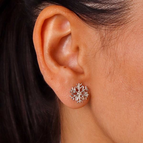 Close-up of silver snowflake earrings worn on ear