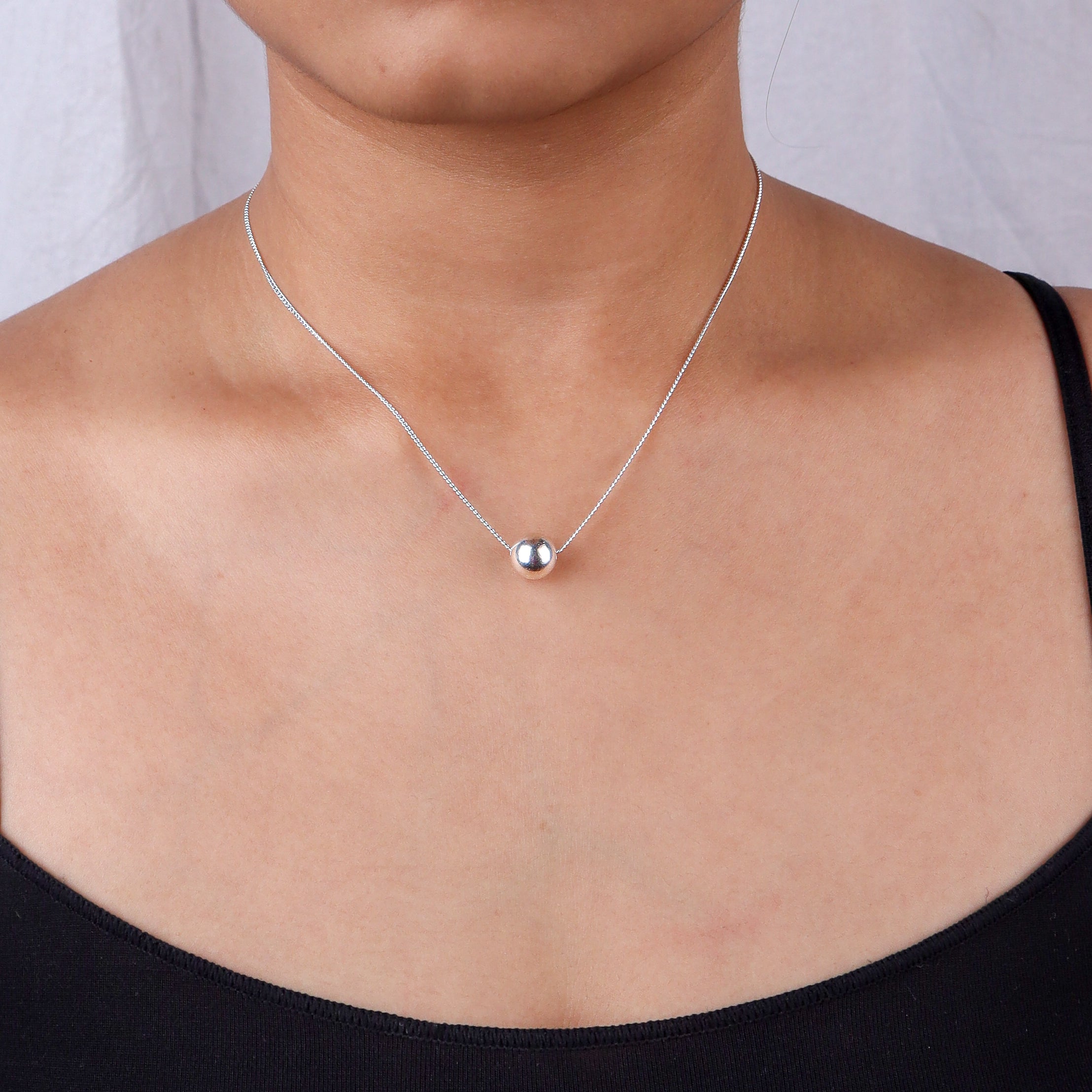 Woman wearing a silver chain necklace with a bead pendant