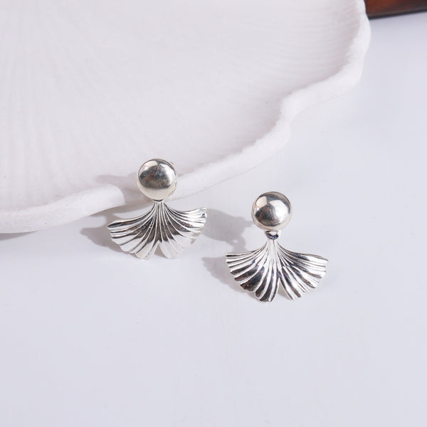 Silver earrings with ginkgo leaf motif on white surface