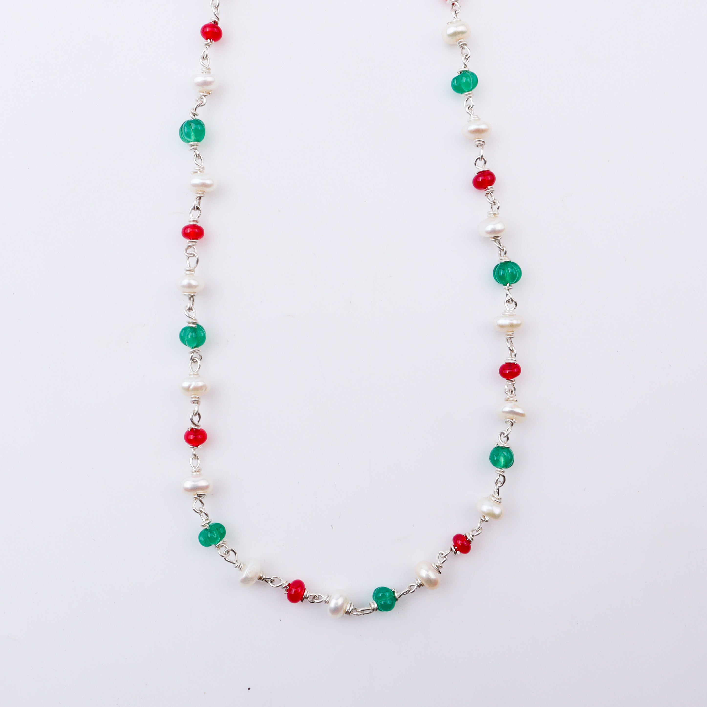 Close-up of beaded necklace with pearls, red and green gemstones on white background