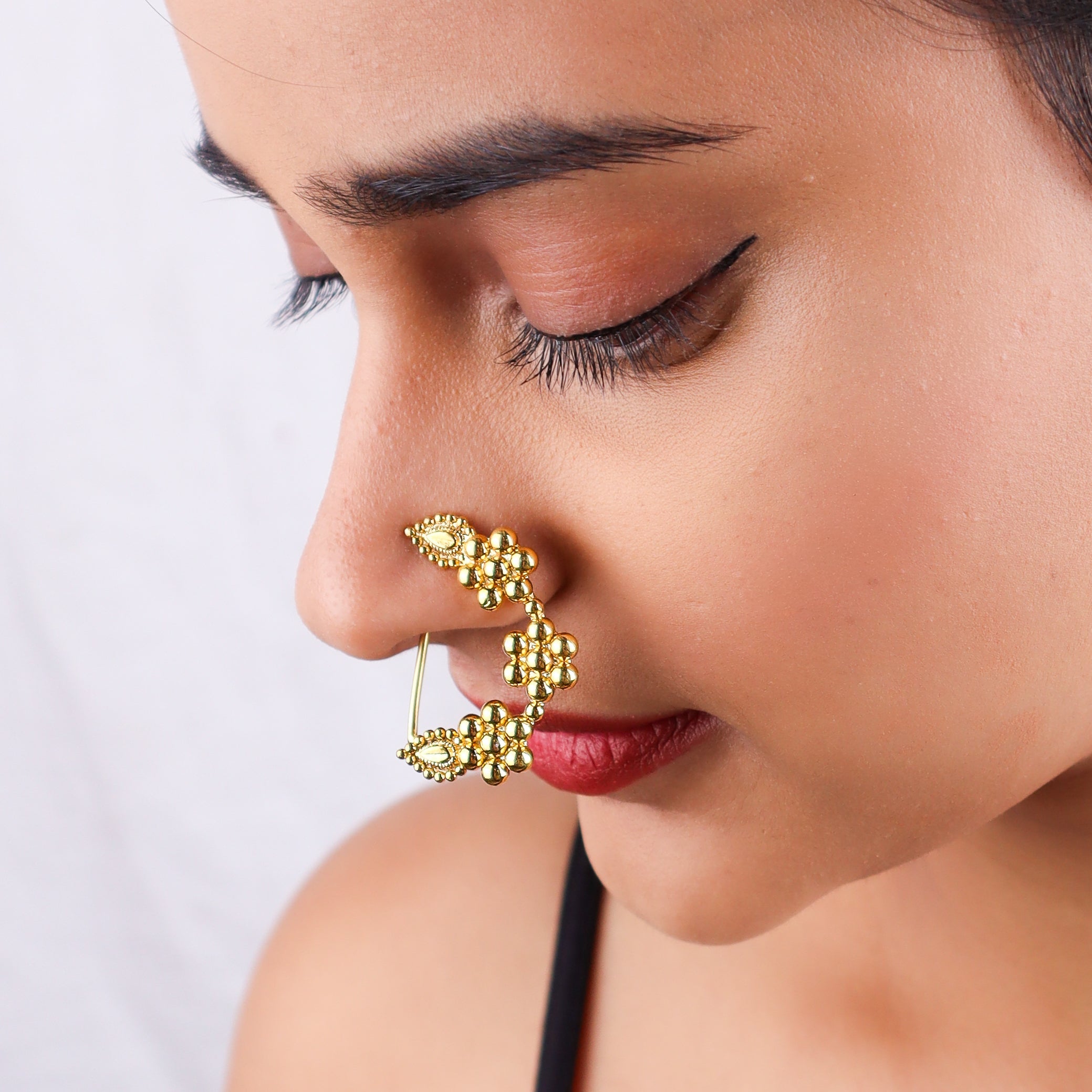 Close-up of gold nose ring on model's nose with detailed craftsmanship