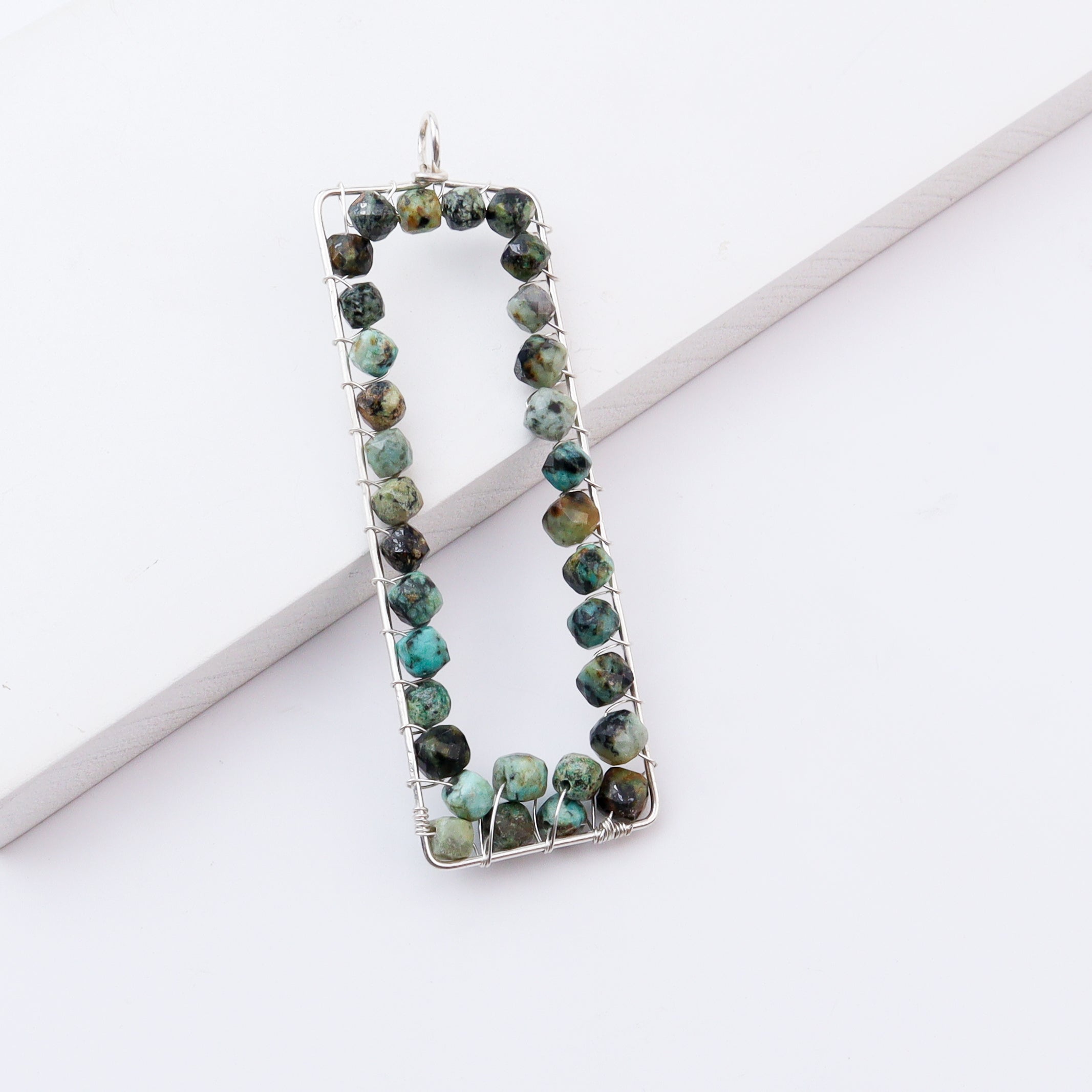 Close-up of rectangular pendant with green and black stones, silver wire wrapping, jewelry accessory
