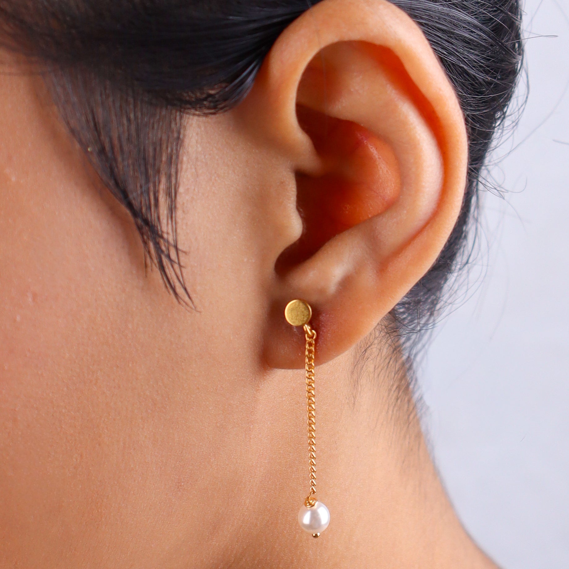 Close-up of gold chain earrings with pearl drops on ear