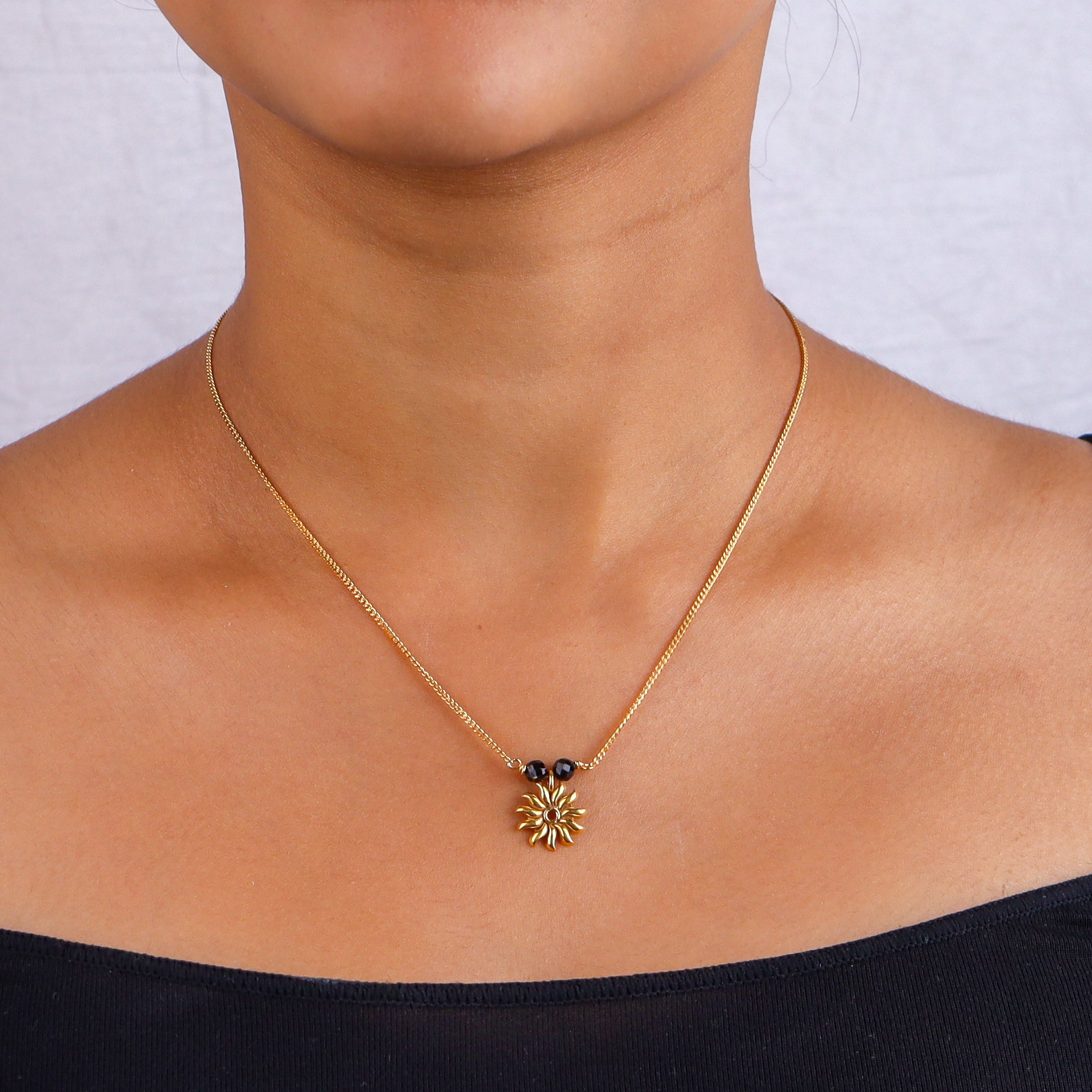 Close-up of gold chain with black beads and sun pendant