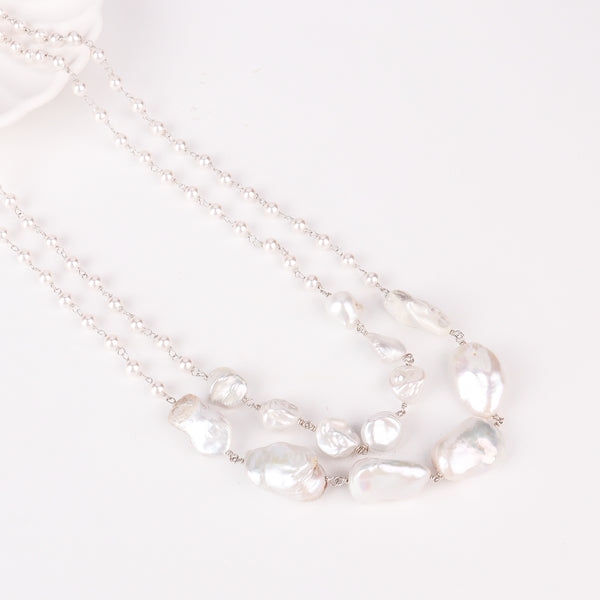 Flat-lay of two layer fresh water pearl necklace with silk fabric and minimal accessories