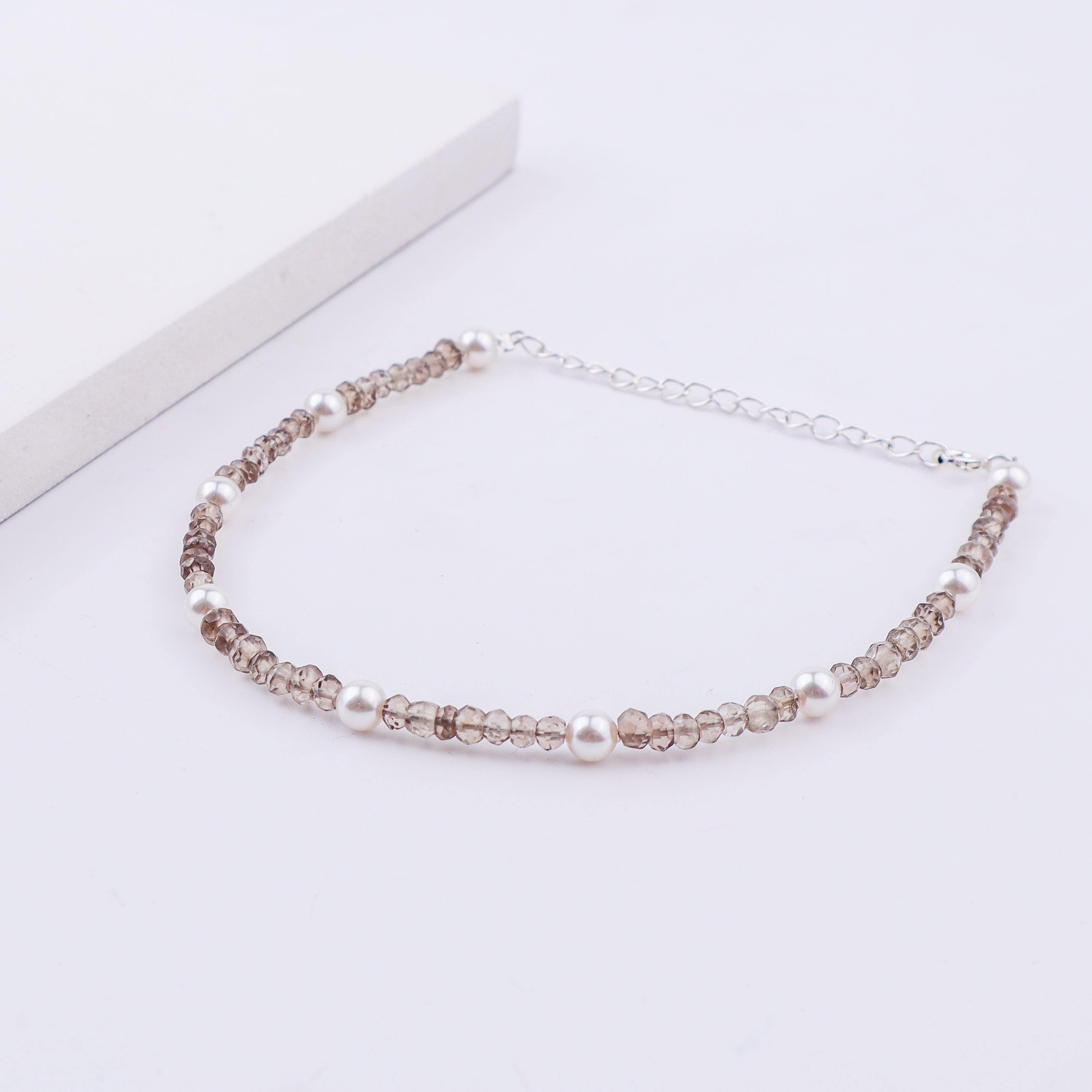 Silver anklet with pearls and faceted beads on white surface