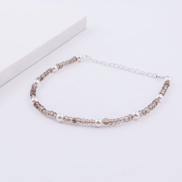 Silver anklet with pearls and faceted beads on white surface