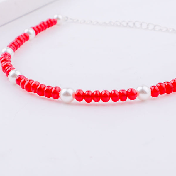 Red and white beaded anklet with silver beads on white background