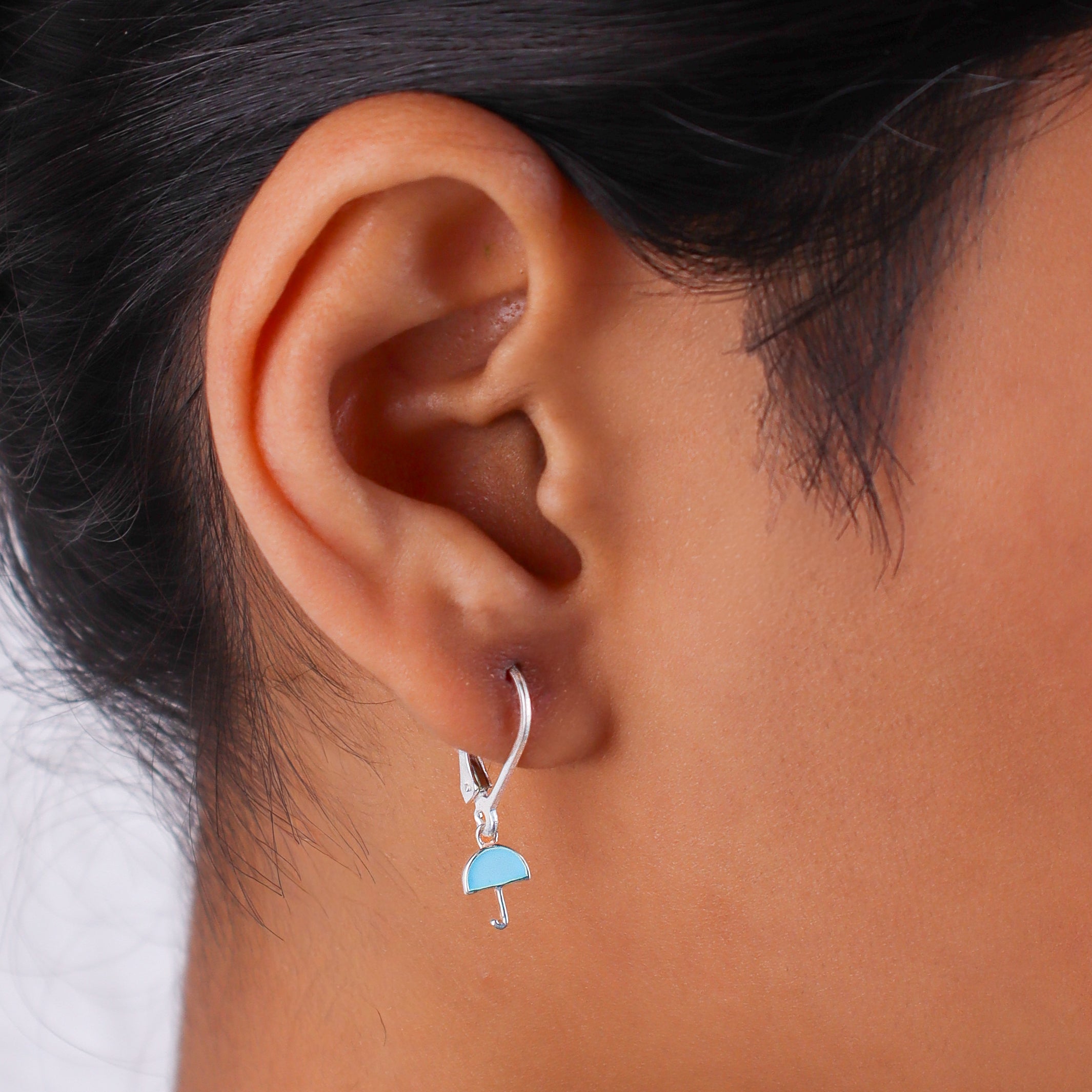 Earrings worn by a woman showing silver enamel umbrella design