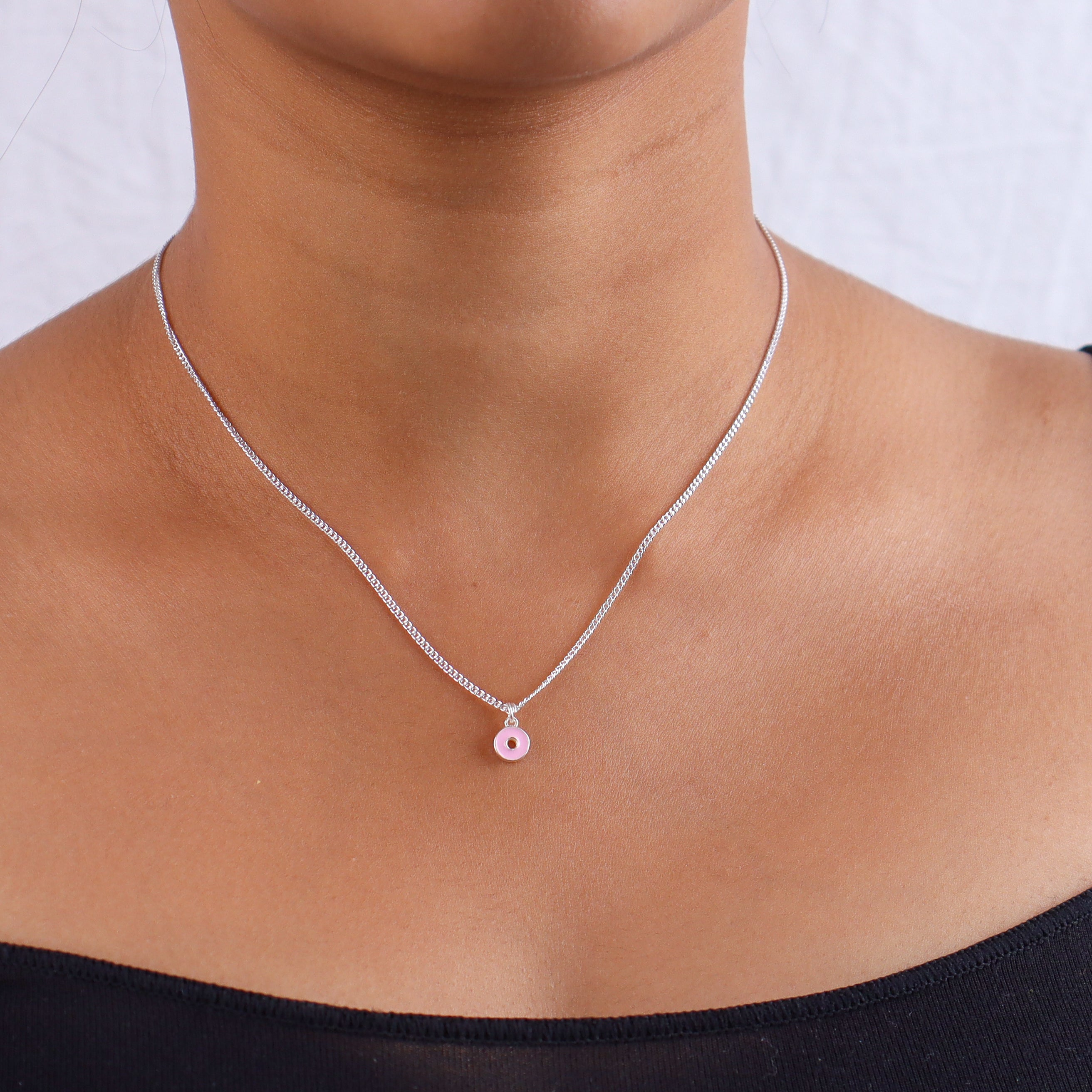 Silver necklace with pink enamel donut pendant on skin