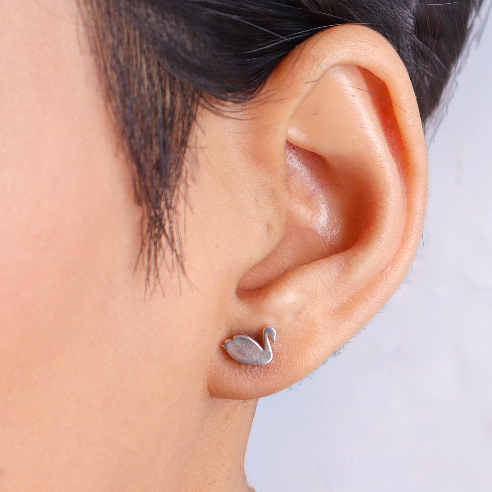 Woman wearing silver swan stud earrings with black hair