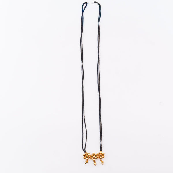 Black beaded necklace with gold pendant on white surface