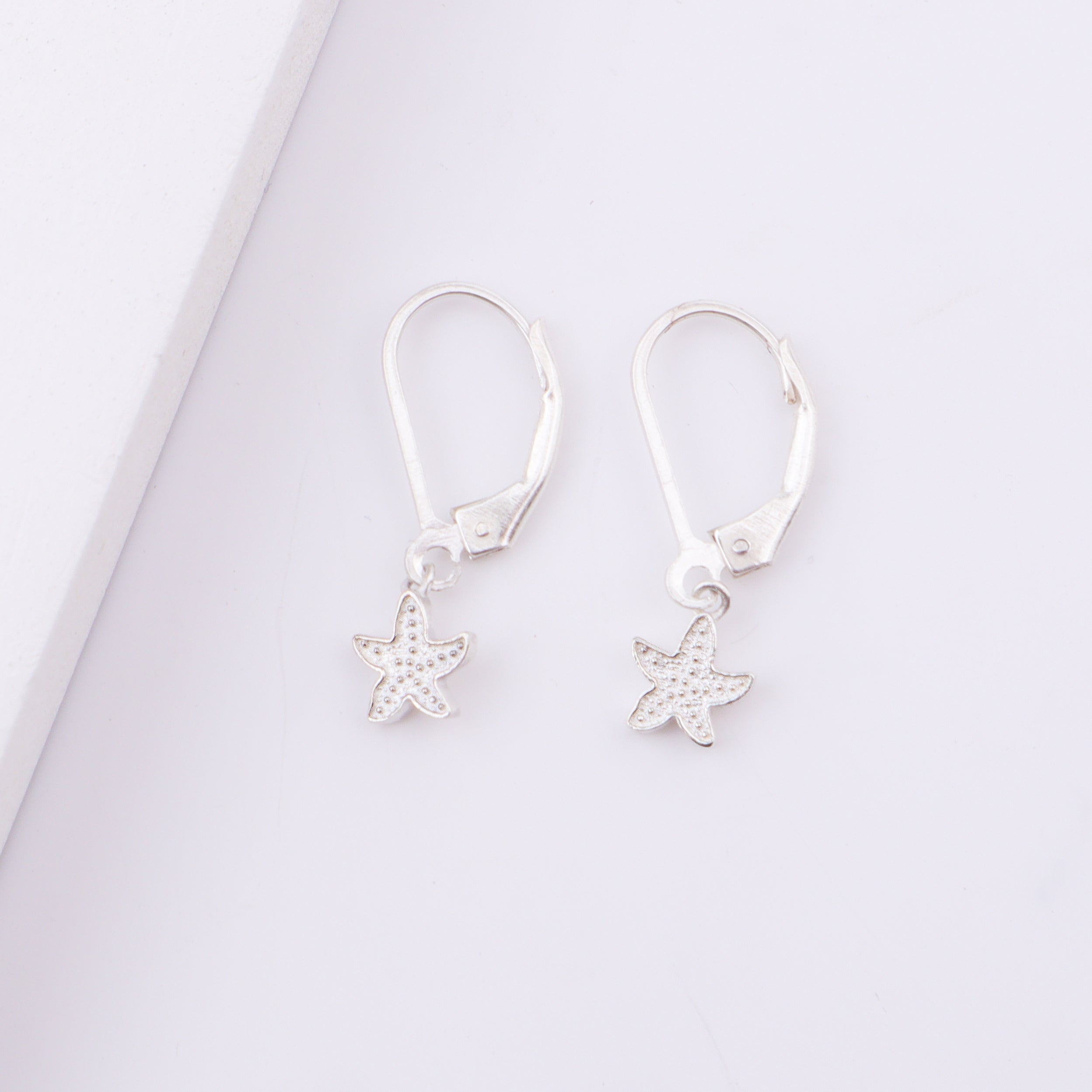 Earrings with starfish charms on white surface