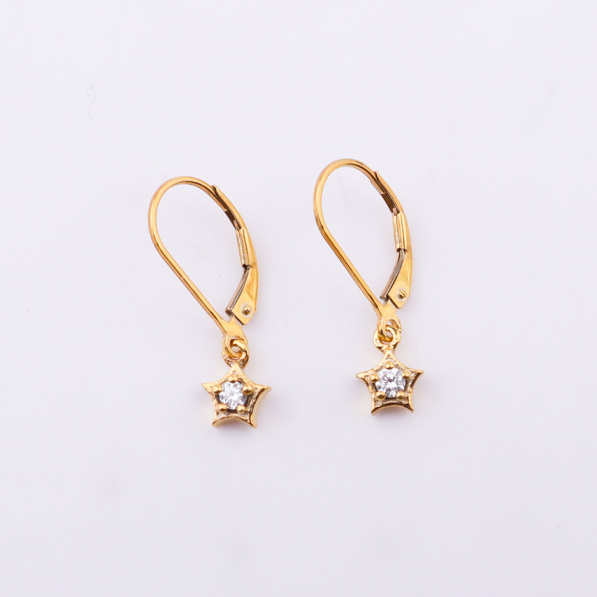 Gold star earrings with cubic zirconia stones on white surface