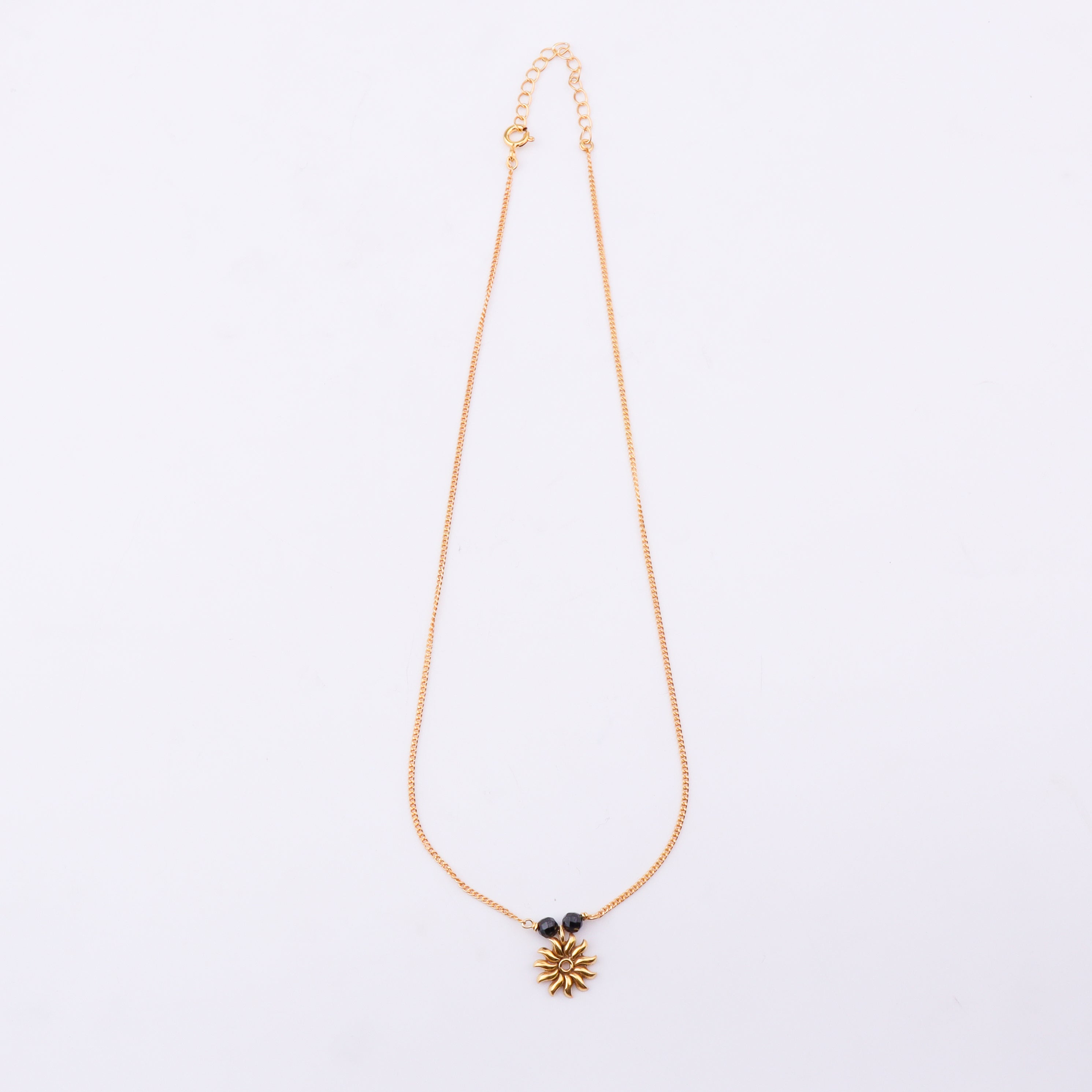 Gold chain with black beads and sun pendant on white background