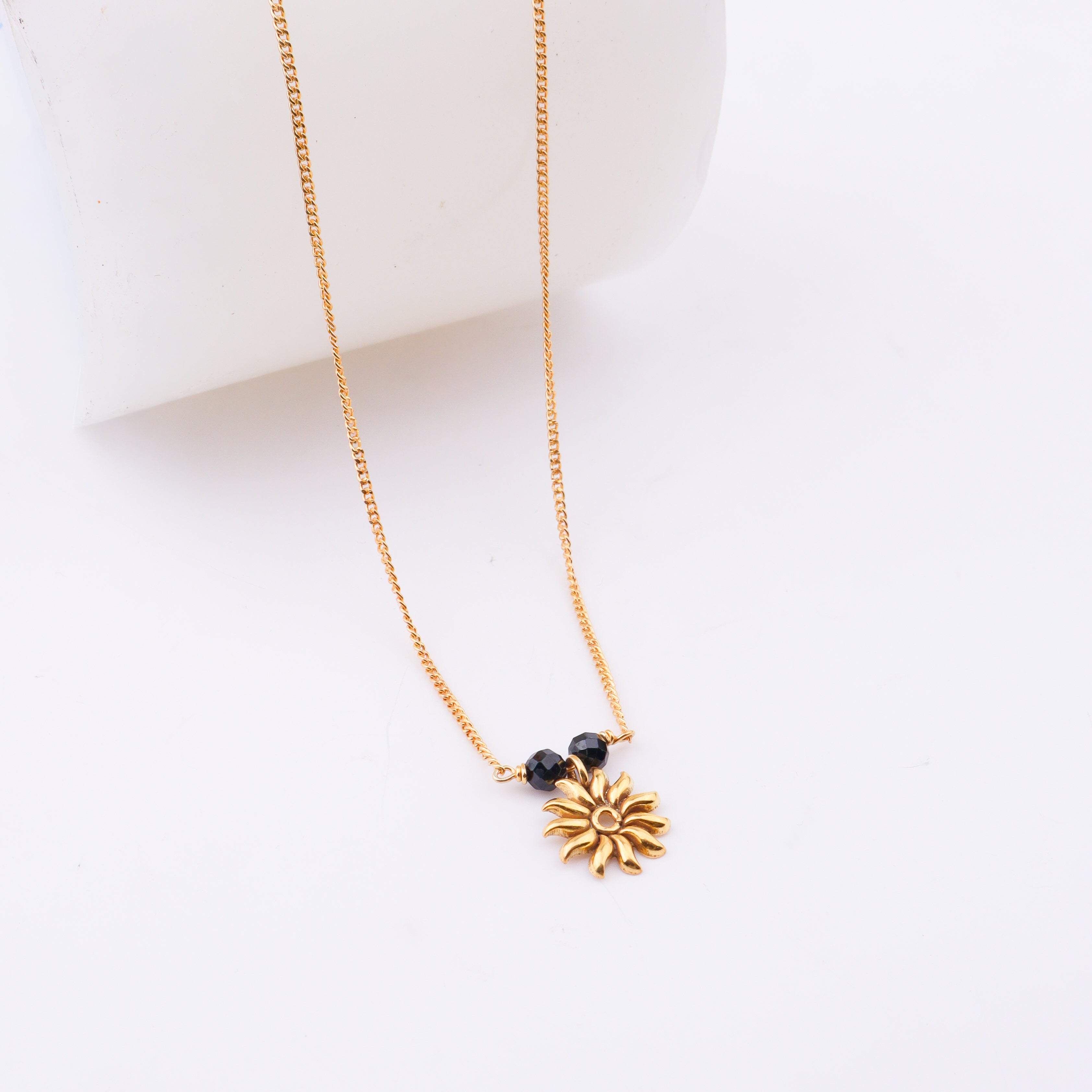 Gold chain with black beads and sun pendant on white surface