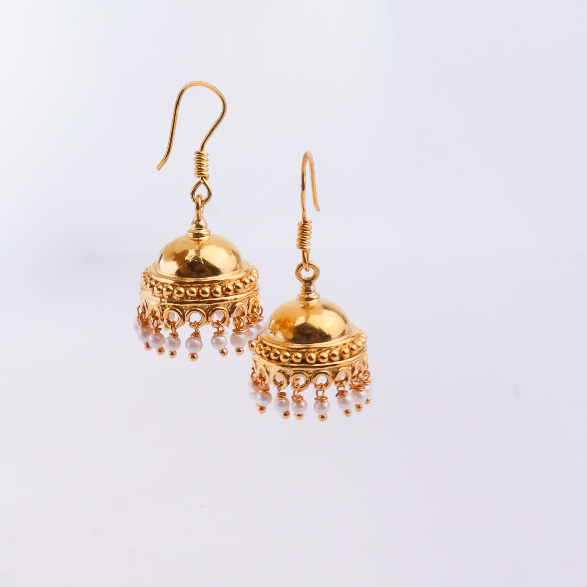 Gold earrings with pearl embellishments on white surface