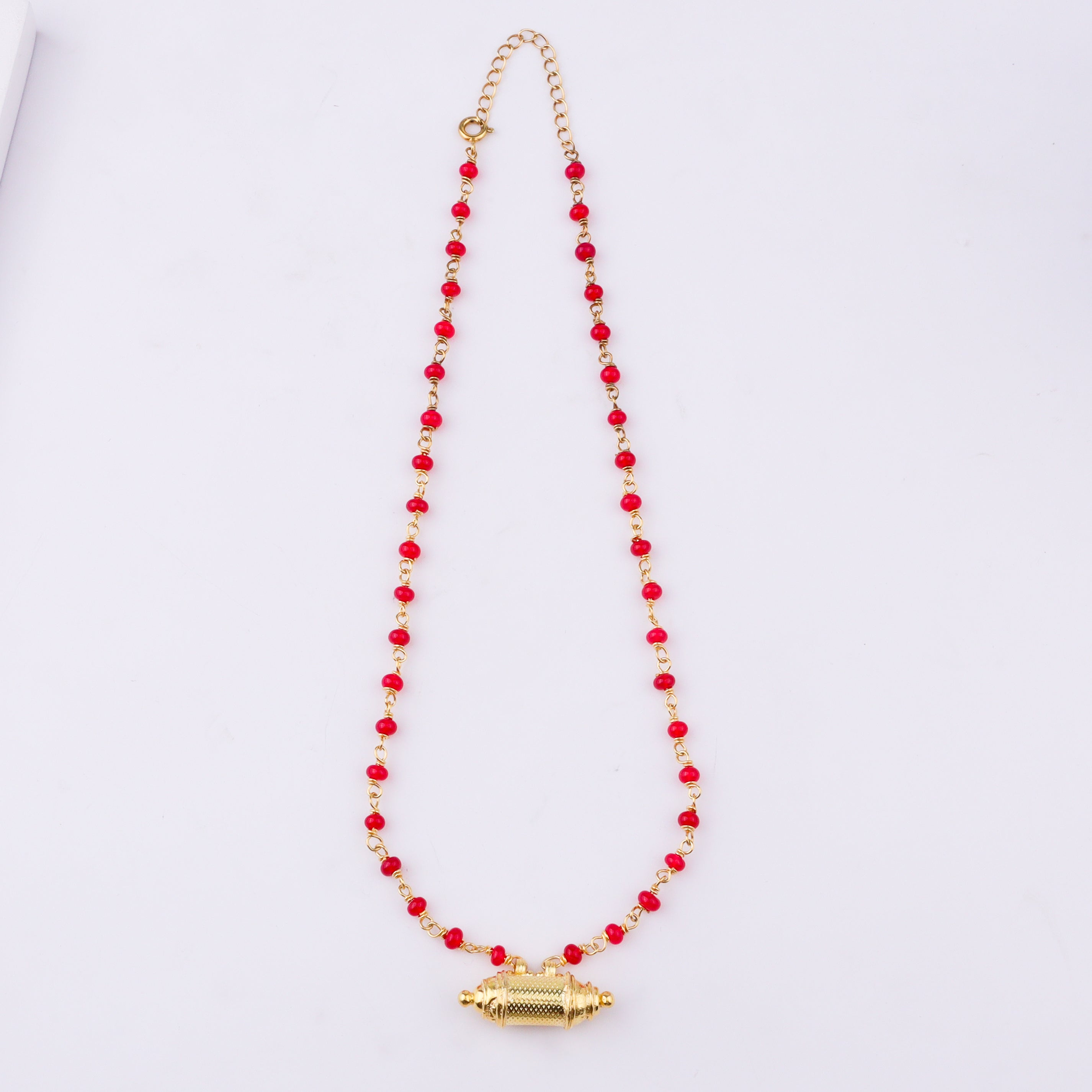 Gold chain with red beads and pendant on white background