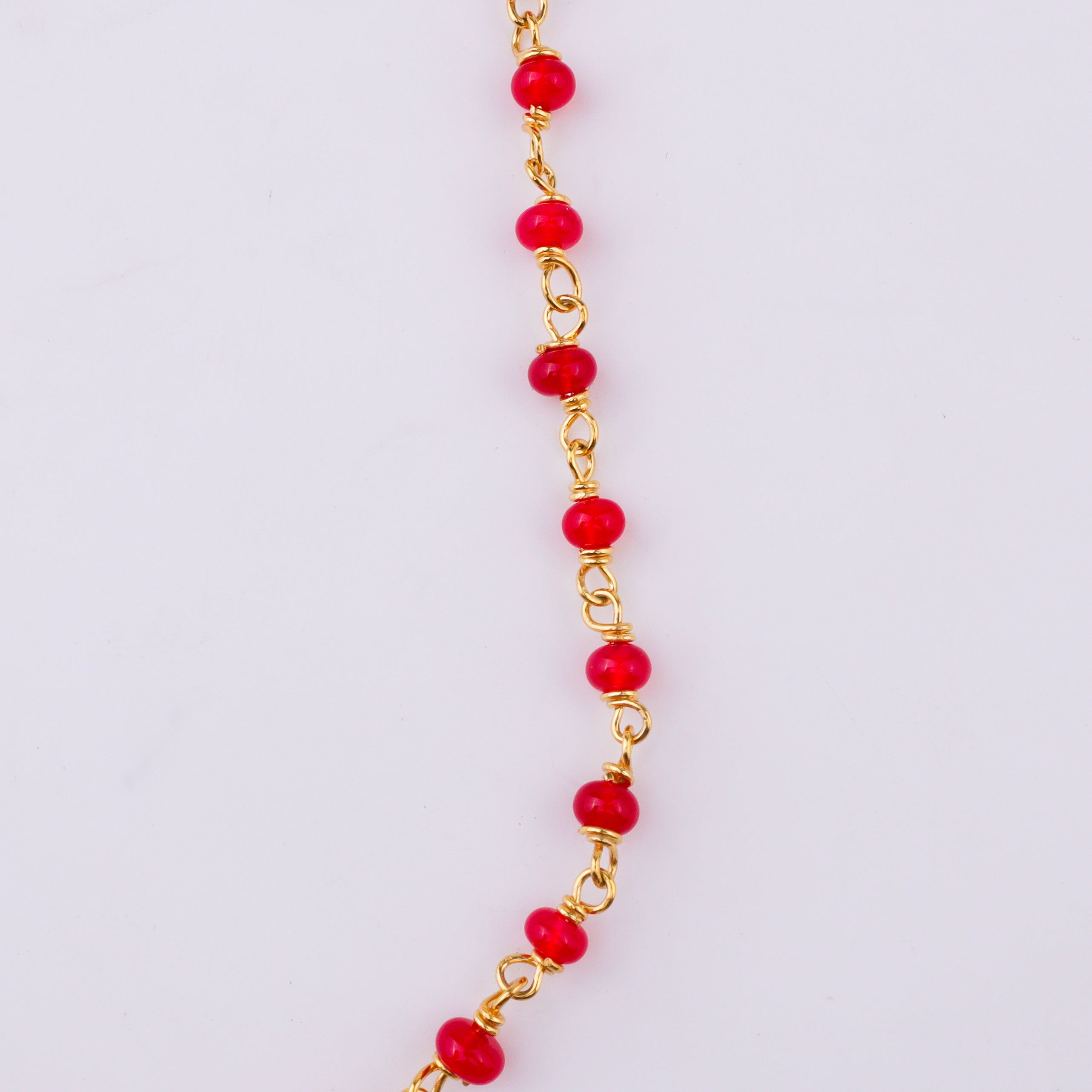 Red beaded necklace with gold chain on white surface