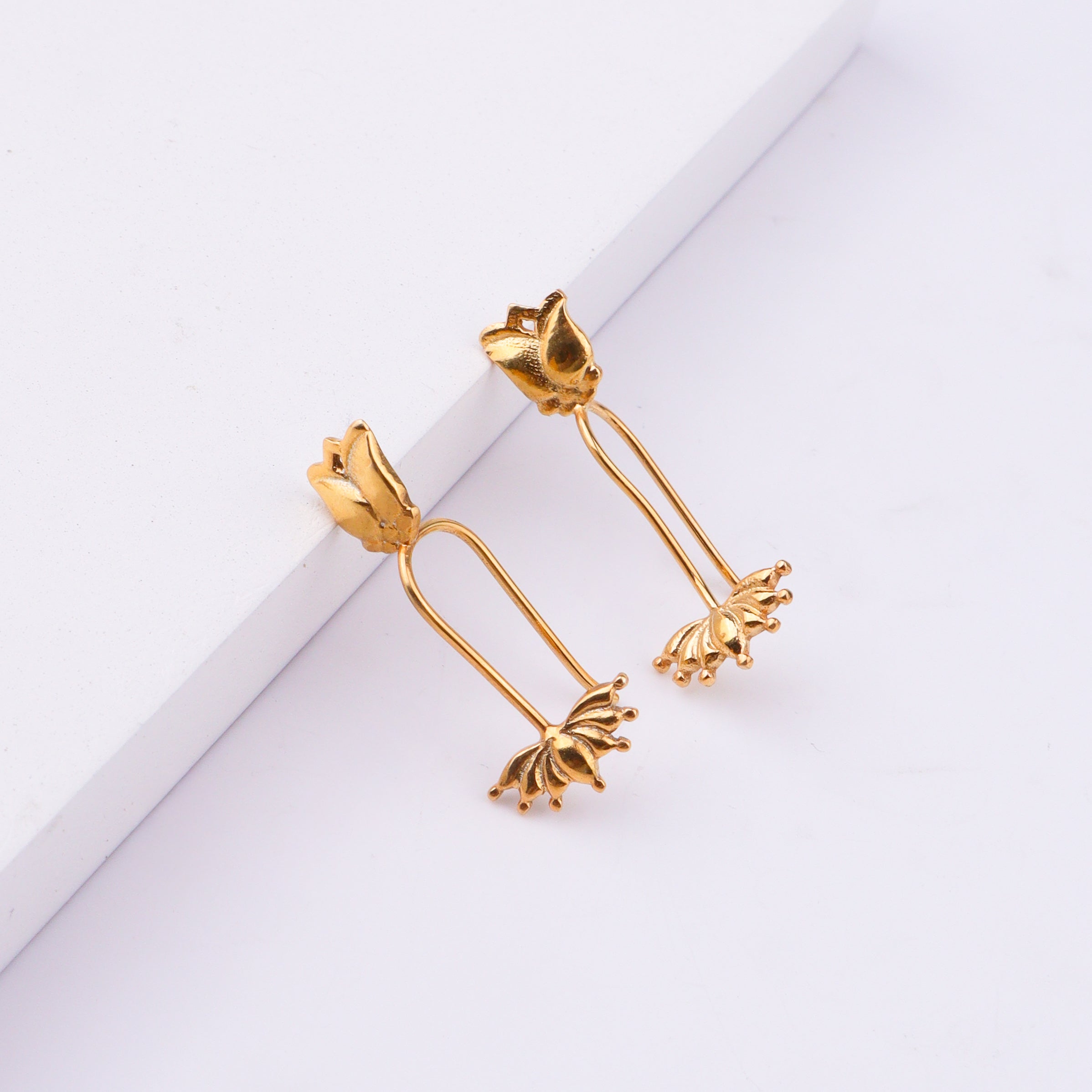 Gold lotus flower earrings displayed on white surface