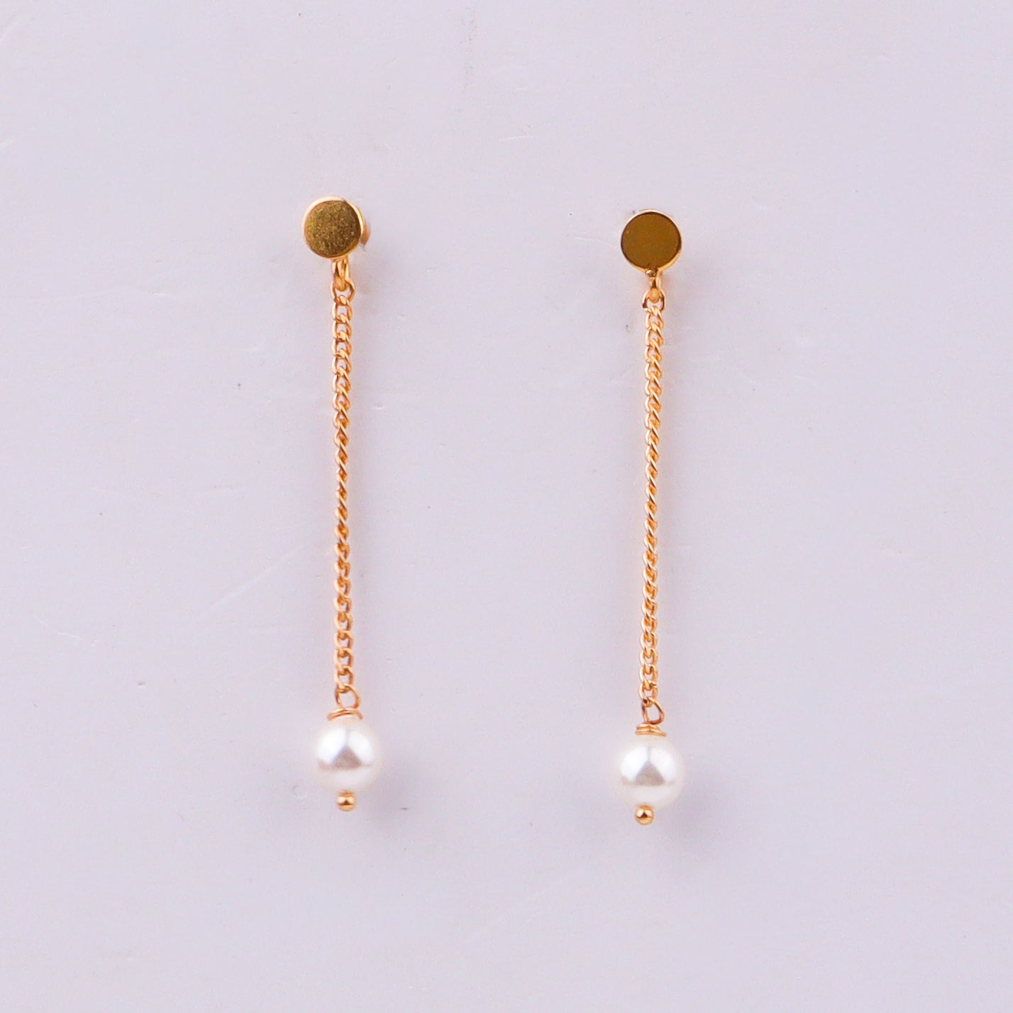 Gold chain earrings with pearl drops on white background