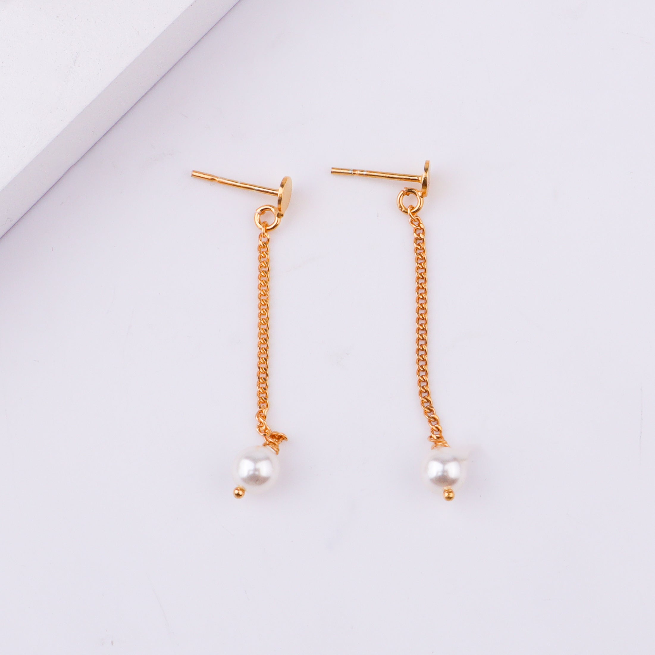 Gold chain earrings with pearl drops on white surface