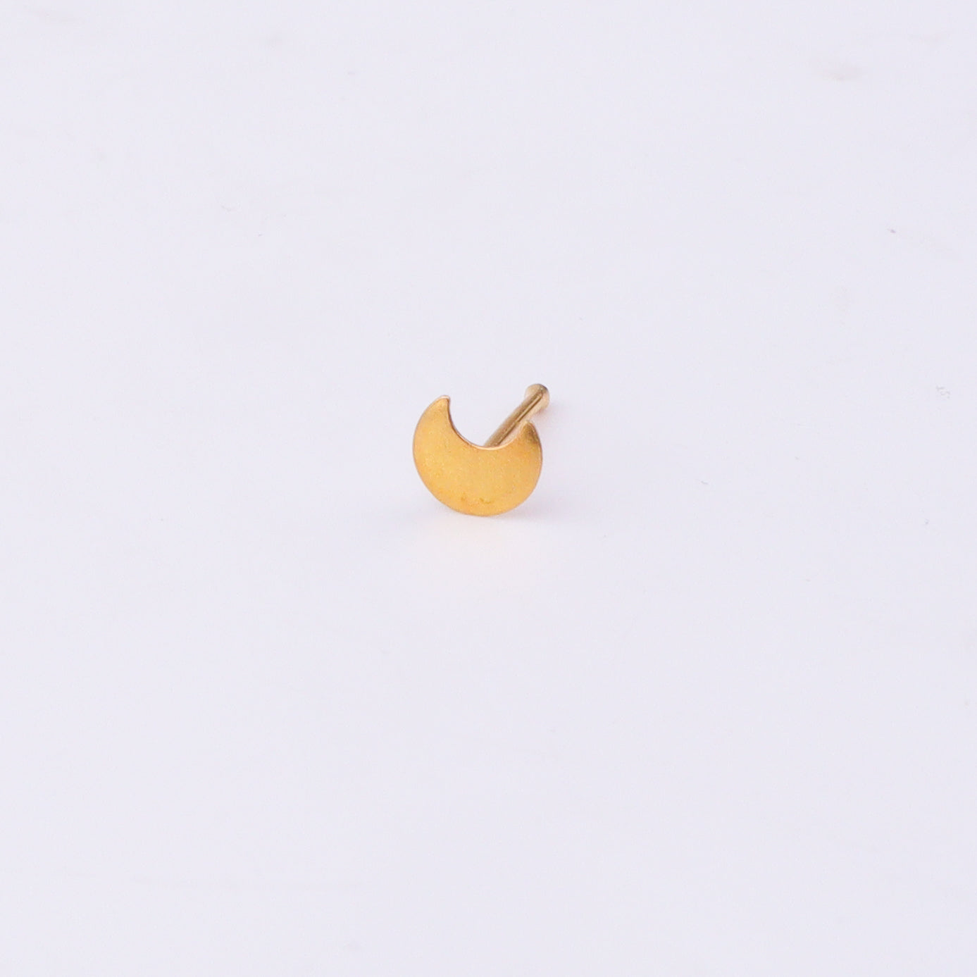 Close-up of gold-tone crescent moon nose pin on white surface