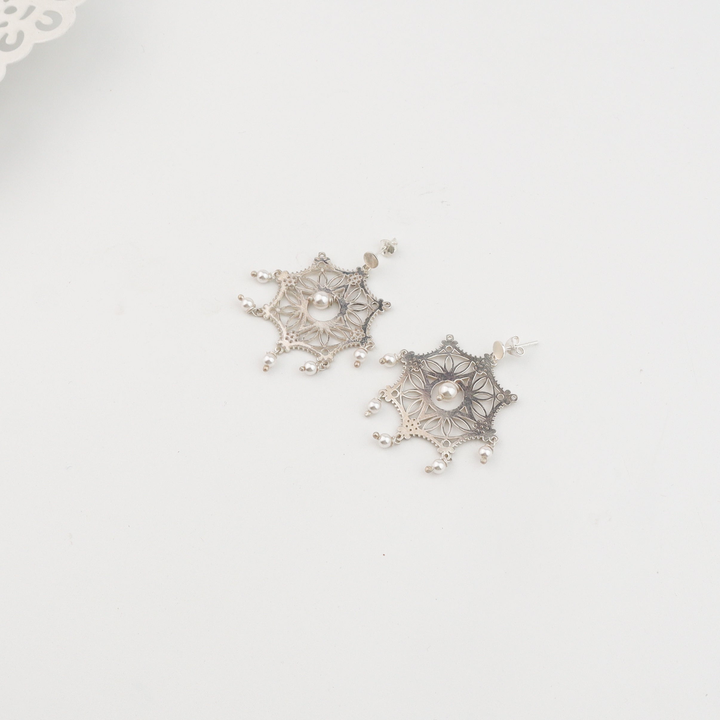 Silver filigree earrings with pearls on white surface