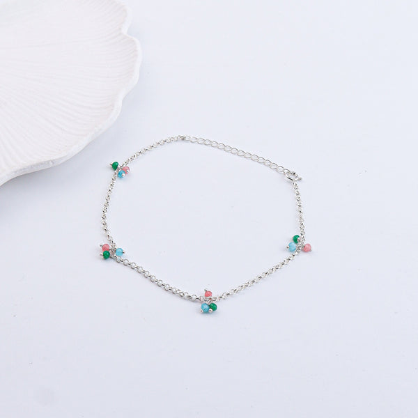 Close-up of silver anklet with beads on white surface