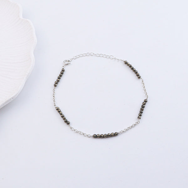 Silver and black beaded anklet on white fabric surface