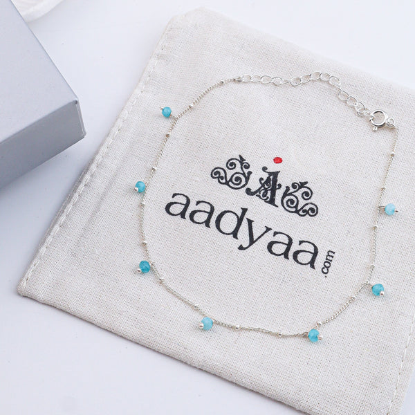 Close-up of silver anklet with blue beads on a white surface