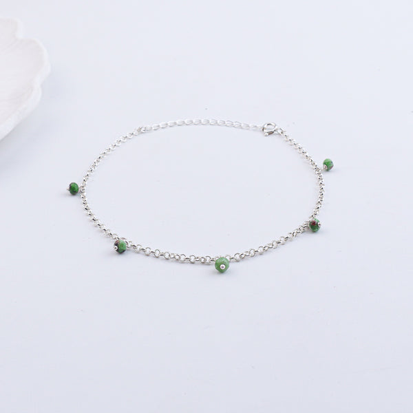 Silver anklet with green beads on white surface