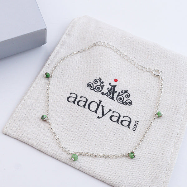 Silver anklet with green beads on white fabric