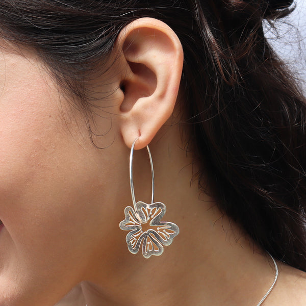 Close-up of silver hoop earrings with flower motif, worn on ear, jewelry accessory