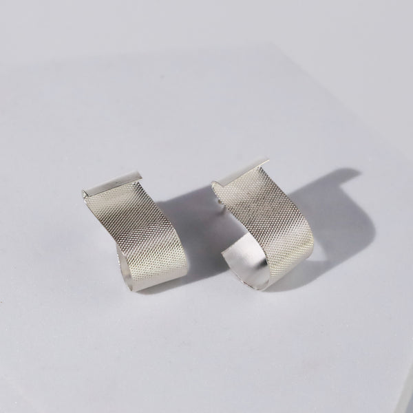 Close-up of textured silver earrings on display