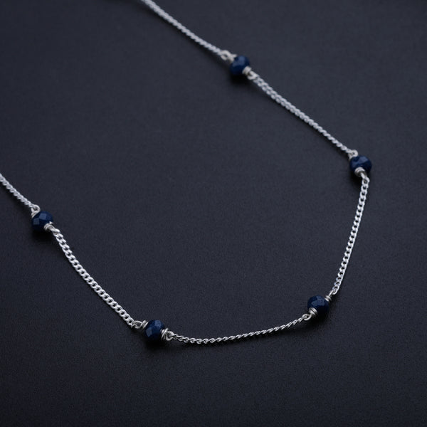 Silver chain necklace with navy blue beads on black background