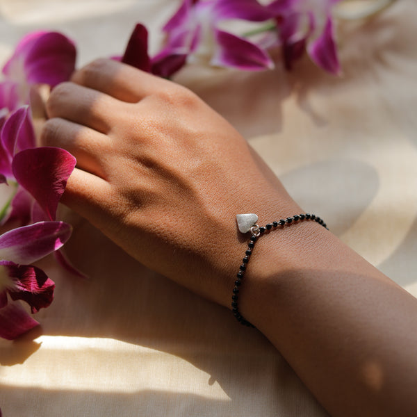 Silver charm mangalsutra bracelet on hand with pink flowers