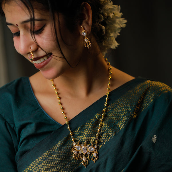 Traditional gold and silver jewelry set with necklace and earrings worn with green saree