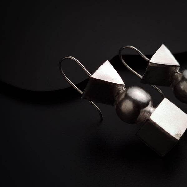 a pair of silver earrings sitting on top of a black surface
