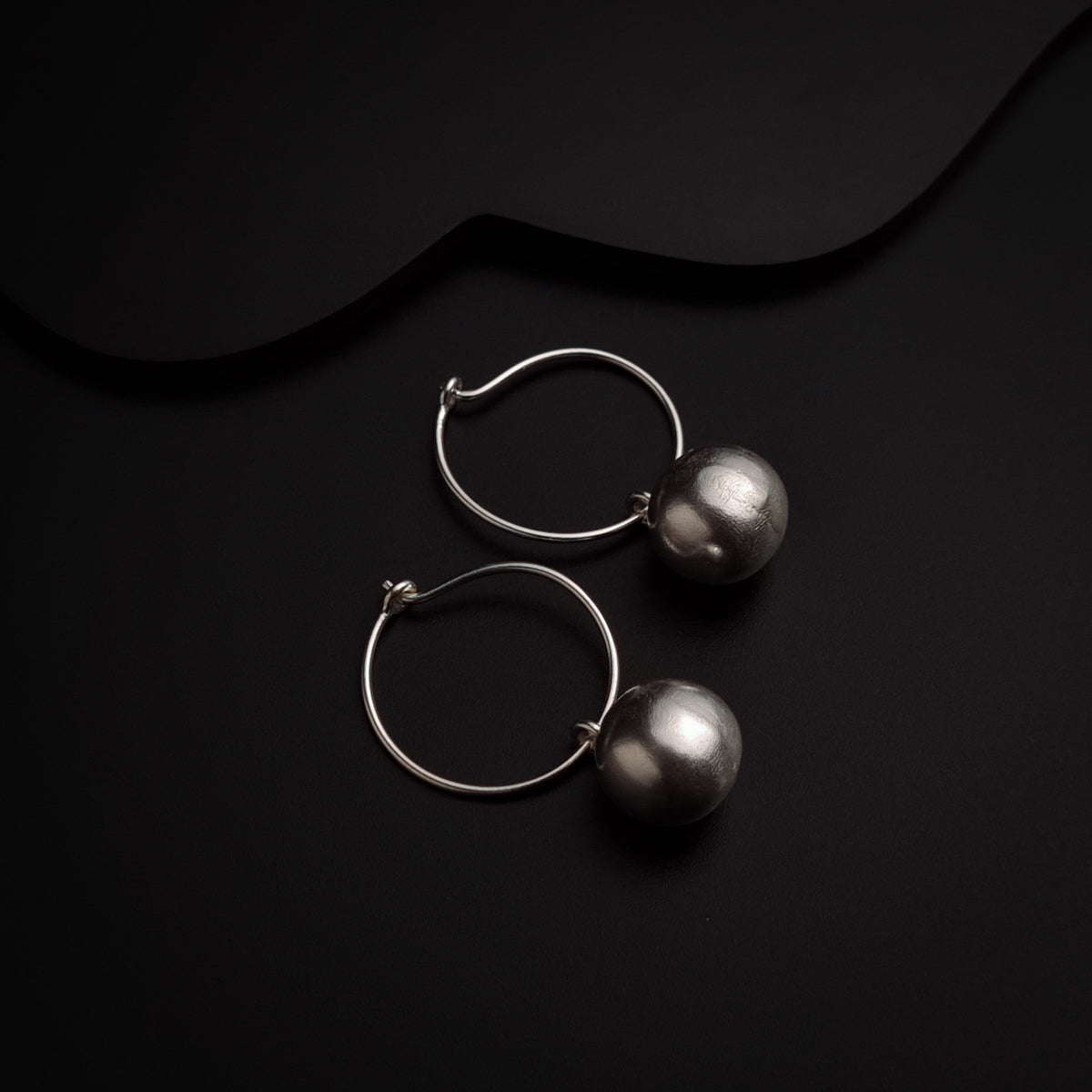 a pair of silver earrings sitting on top of a black surface
