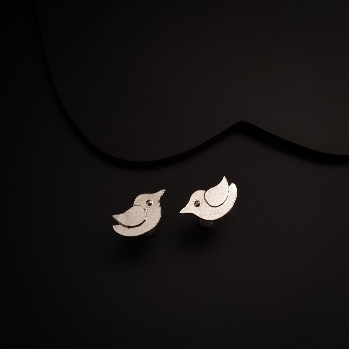 a pair of bird earrings sitting on top of a black surface